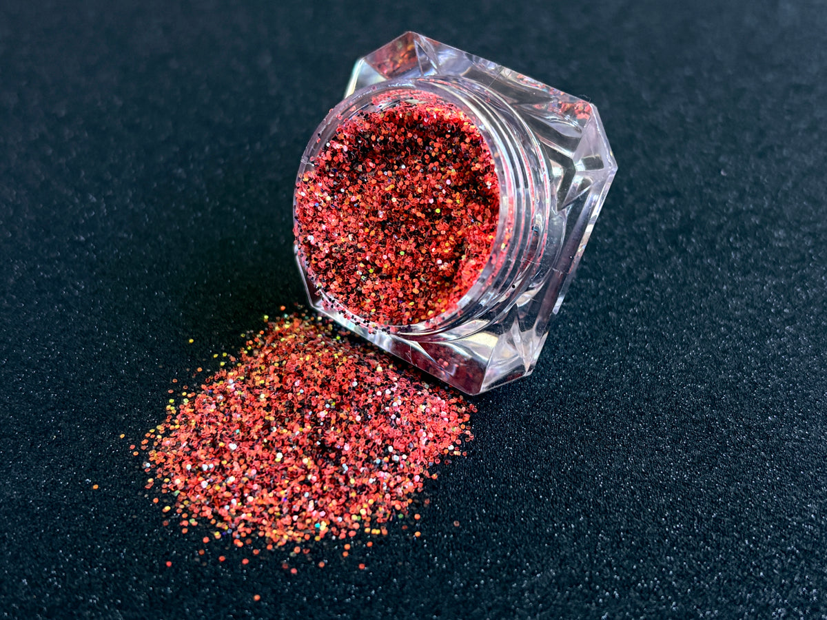 Bright coral and black glitter with holographic and iridescent sparkle spilled from a clear jar onto a black textured background.