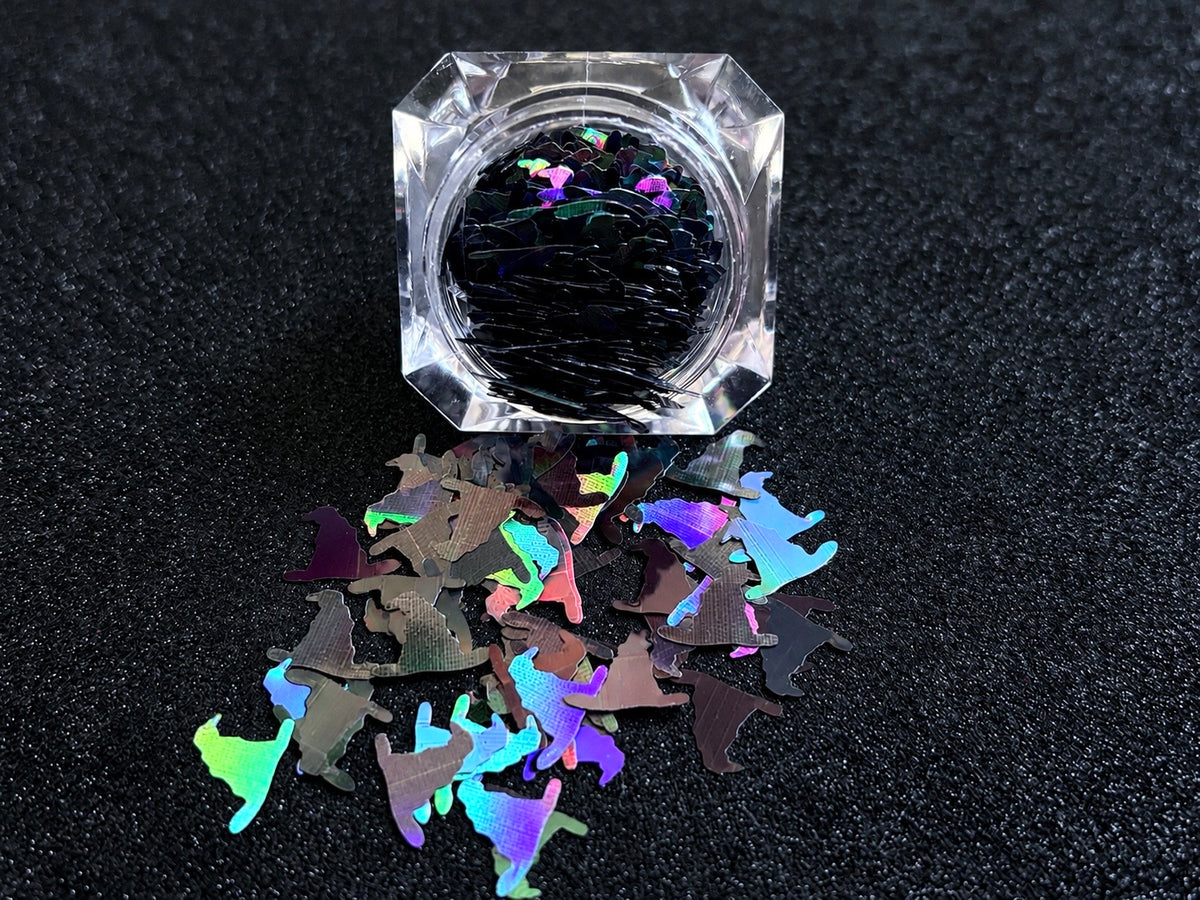 10mm holographic black witch hat glitter shapes spilled from a clear jar onto a black textured background.
