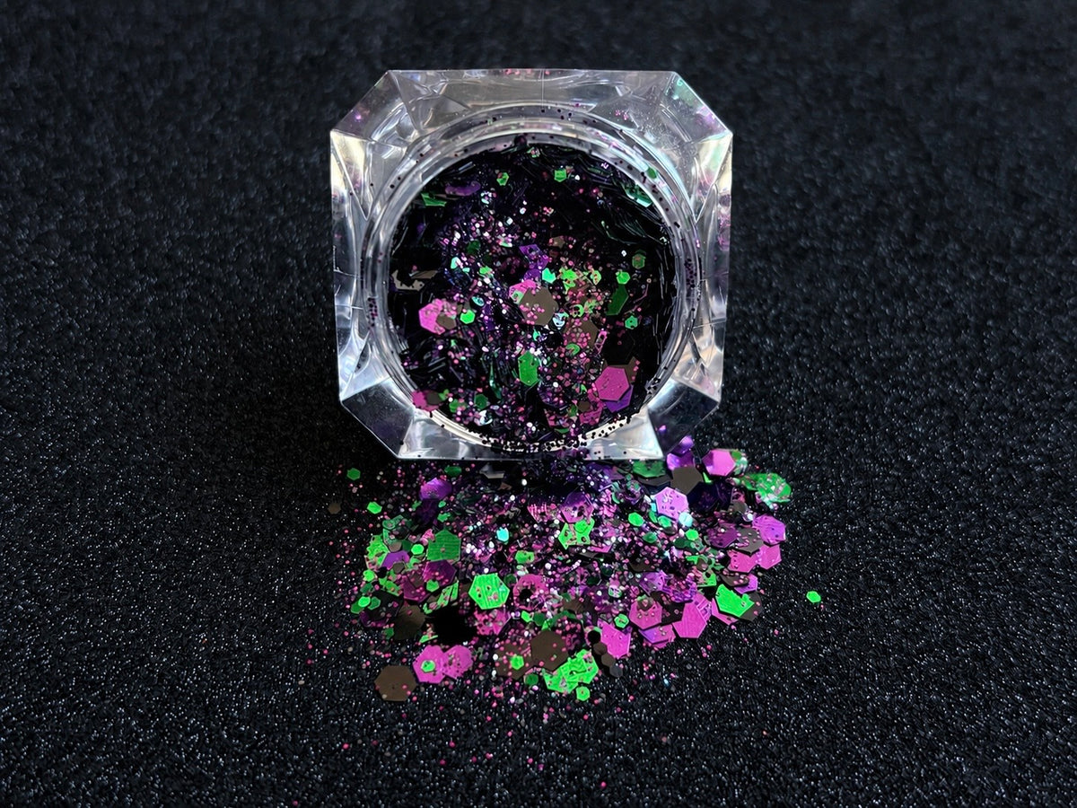 Emerald green, dark purple, and black metallic glitter mix spilled from a clear jar onto a black textured background.