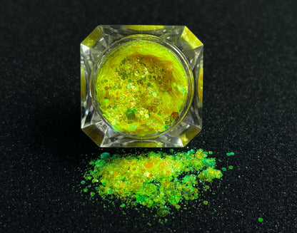 Fluorescent iridescent green super chunky glitter mix with yellow shift spilled from a clear jar onto a black textured background.