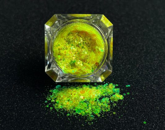 Fluorescent iridescent green super chunky glitter mix with yellow shift spilled from a clear jar onto a black textured background.