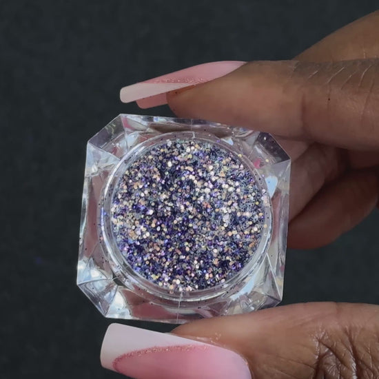 Purple and gold glitter mix in a clear jar, tilted back and forth to show sparkle against a black background.