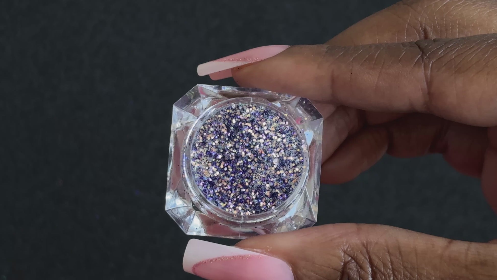 Purple and gold glitter mix in a clear jar, tilted back and forth to show sparkle against a black background.