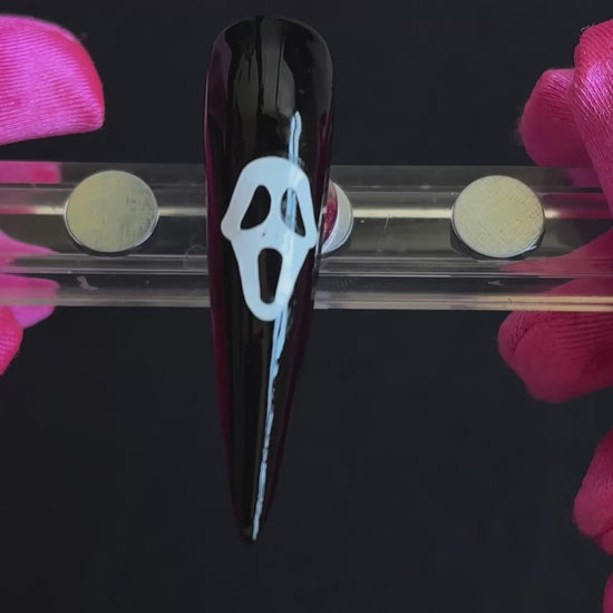 White Ghostface Halloween nail sticker on a glossy black stiletto nail tip, tilted back and forth to show the finished nail design.