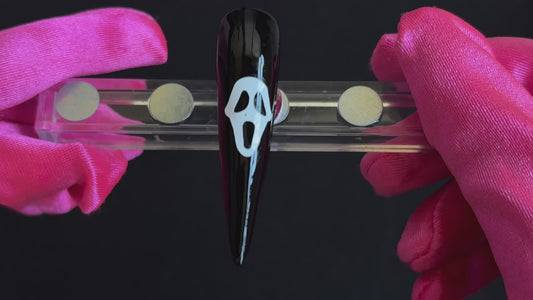 White Ghostface Halloween nail sticker on a glossy black stiletto nail tip, tilted back and forth to show the finished nail design.