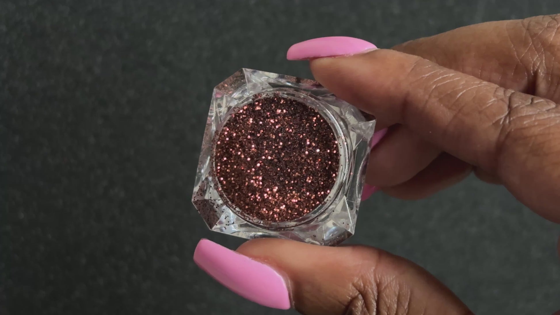 Chocolate brown metallic glitter in a clear jar, tilted back and forth to show sparkle against a black background.