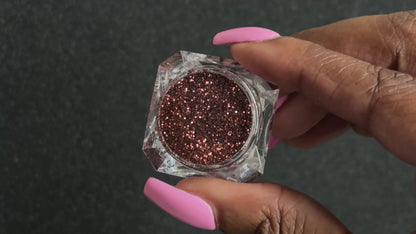 Chocolate brown metallic glitter in a clear jar, tilted back and forth to show sparkle against a black background.