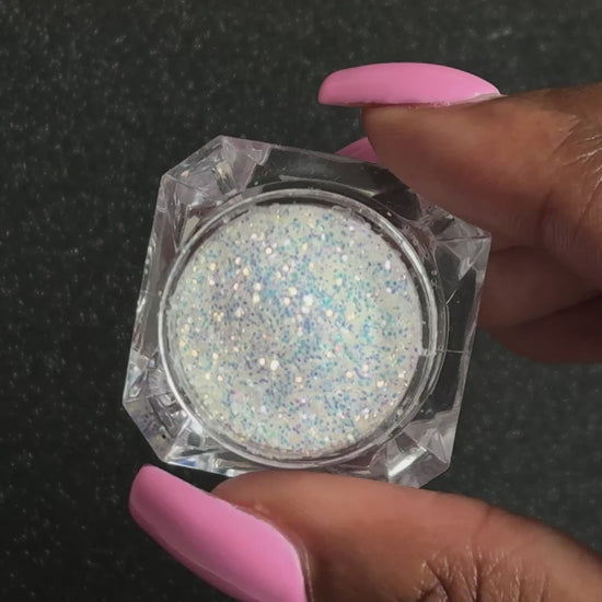 Blue-purple and gold glitter mix in a clear jar, tilted back and forth to show sparkle against a black background. 
