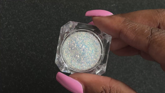 Blue-purple and gold glitter mix in a clear jar, tilted back and forth to show sparkle against a black background. 