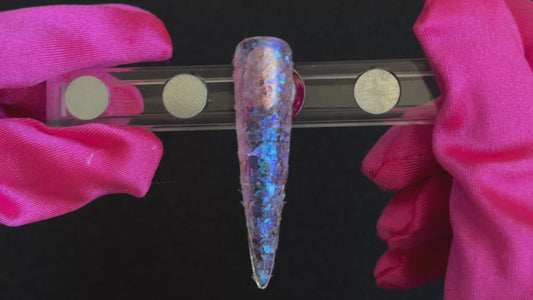 Iridescent white cellophane glitter flakes with purple reflections applied on a stiletto nail tip, tilted to show sparkle.