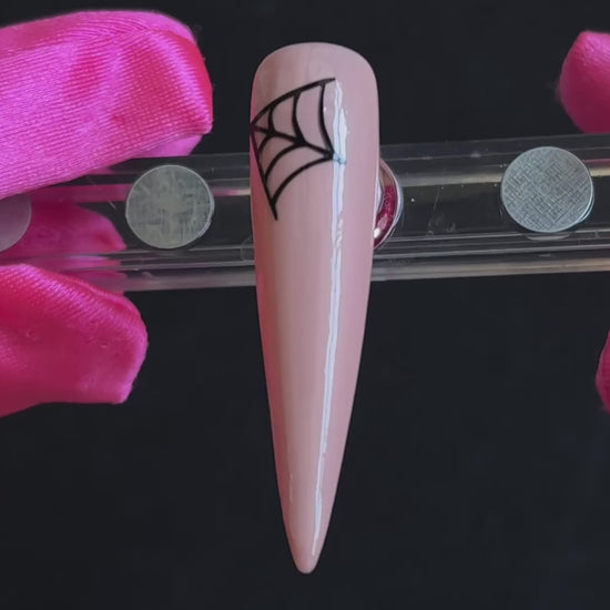 Black cobweb Halloween nail sticker on a glossy nude stiletto nail tip, tilted back and forth to show the finished nail design.
