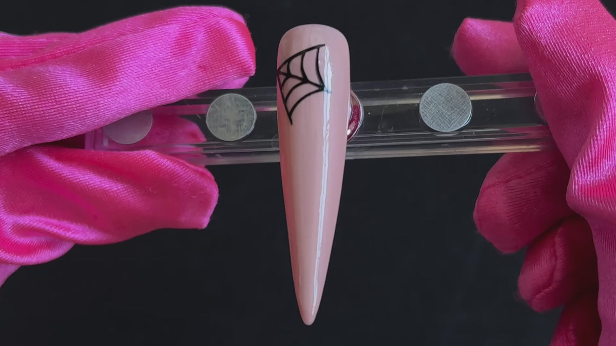 Black cobweb Halloween nail sticker on a glossy nude stiletto nail tip, tilted back and forth to show the finished nail design.