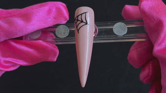 Black cobweb Halloween nail sticker on a glossy nude stiletto nail tip, tilted back and forth to show the finished nail design.