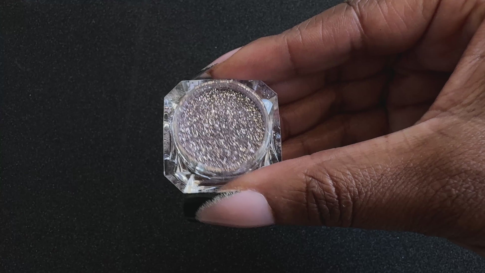 Champagne pink glitter in a clear jar, tilted back and forth to show sparkle against a black background.