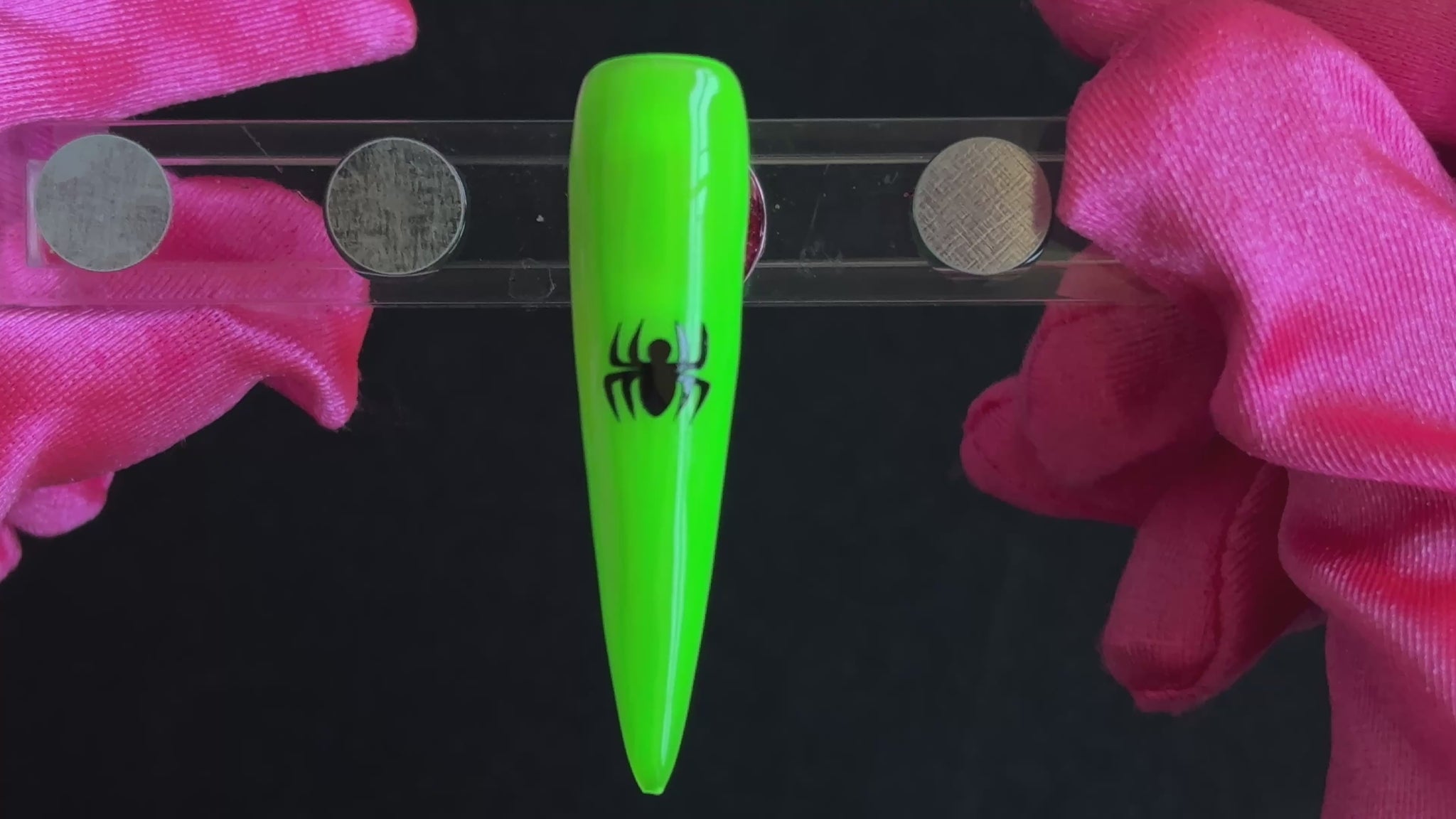 Black spider nail sticker on a bright green stiletto nail tip, tilted back and forth to show the finished nail design.