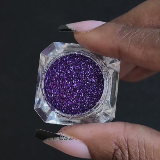 Royal purple metallic glitter in a clear jar, tilted back and forth to show sparkle against a black background.