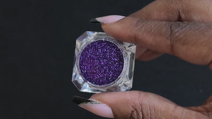 Royal purple metallic glitter in a clear jar, tilted back and forth to show sparkle against a black background.