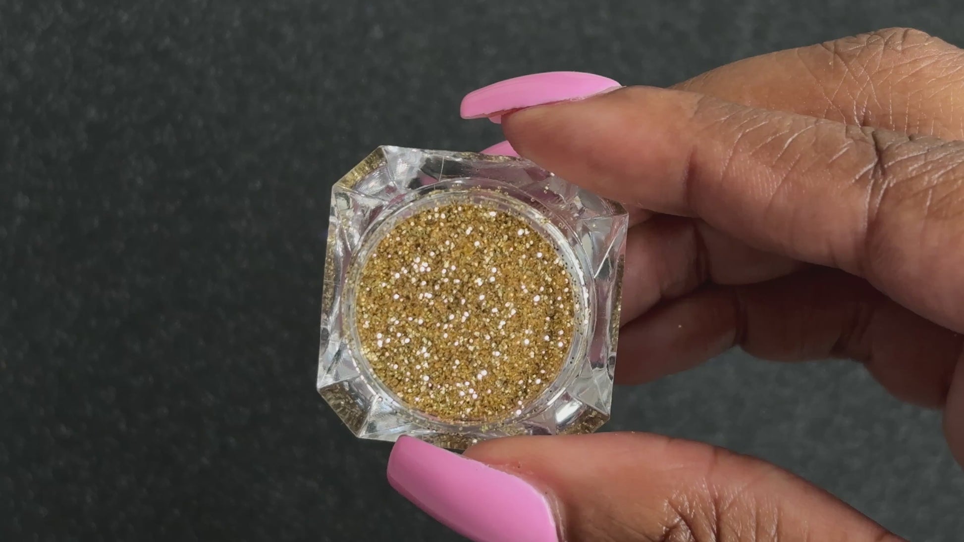 Gold metallic glitter in a clear jar, tilted back and forth to show sparkle against a black background.