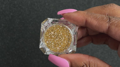 Gold metallic glitter in a clear jar, tilted back and forth to show sparkle against a black background.