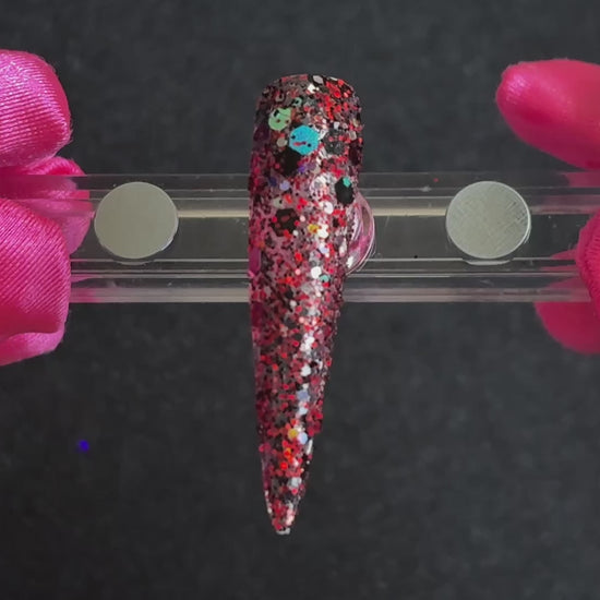 Ruby red, black, silver, and gold holographic super chunky glitter mix applied on a stiletto nail tip, tilted back and forth to show sparkle. 