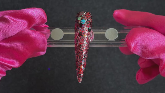 Ruby red, black, silver, and gold holographic super chunky glitter mix applied on a stiletto nail tip, tilted back and forth to show sparkle. 