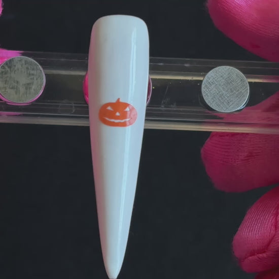Orange pumpkin Halloween nail sticker on a glossy white stiletto nail tip, tilted back and forth to show the finished nail design.