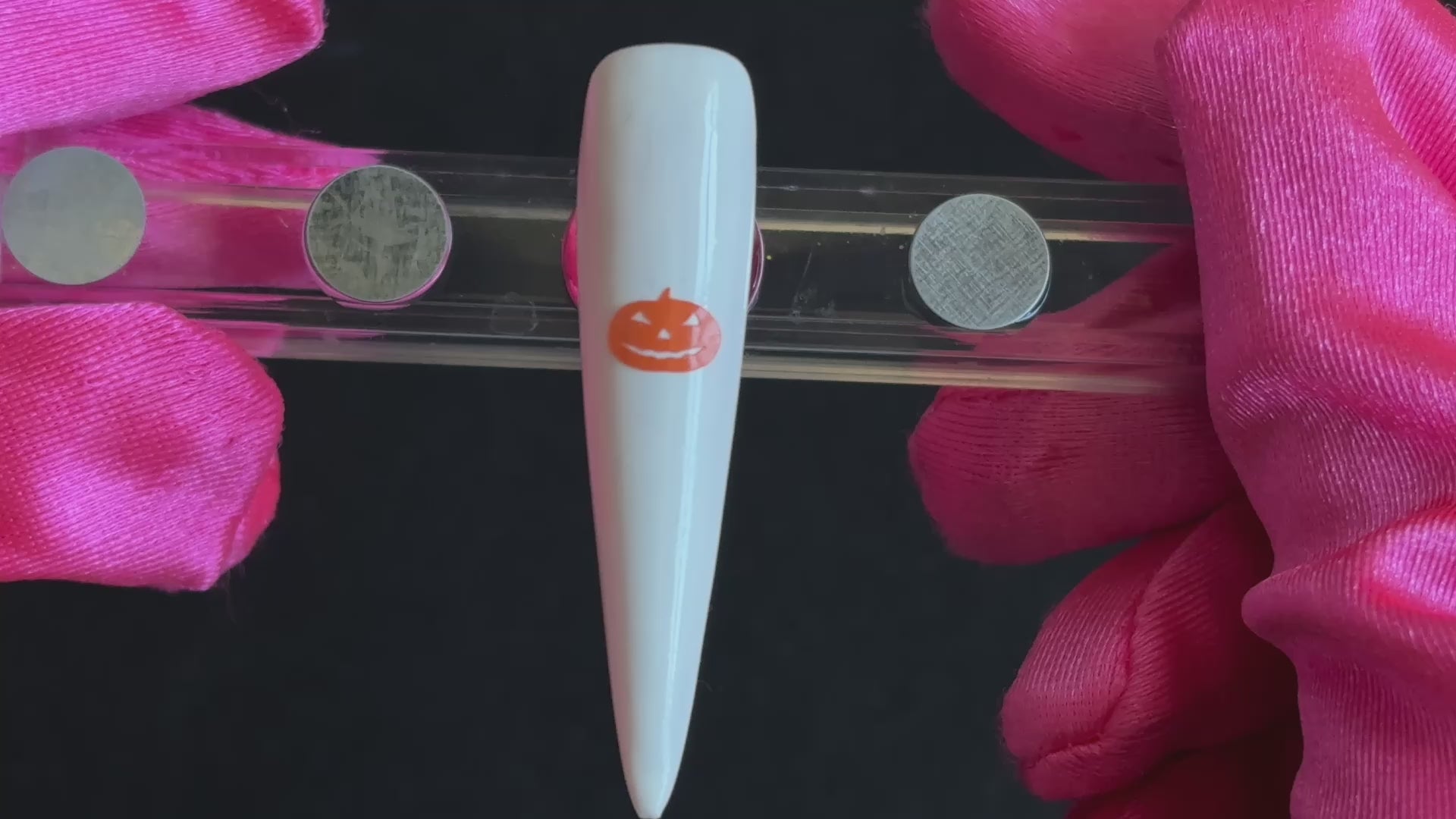 Orange pumpkin Halloween nail sticker on a glossy white stiletto nail tip, tilted back and forth to show the finished nail design.