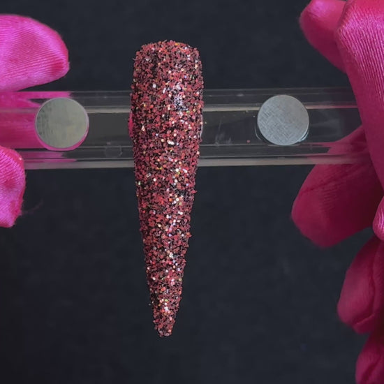 Bright coral and black glitter with holographic and iridescent sparkle applied on a stiletto nail tip, tilted back and forth to show sparkle.