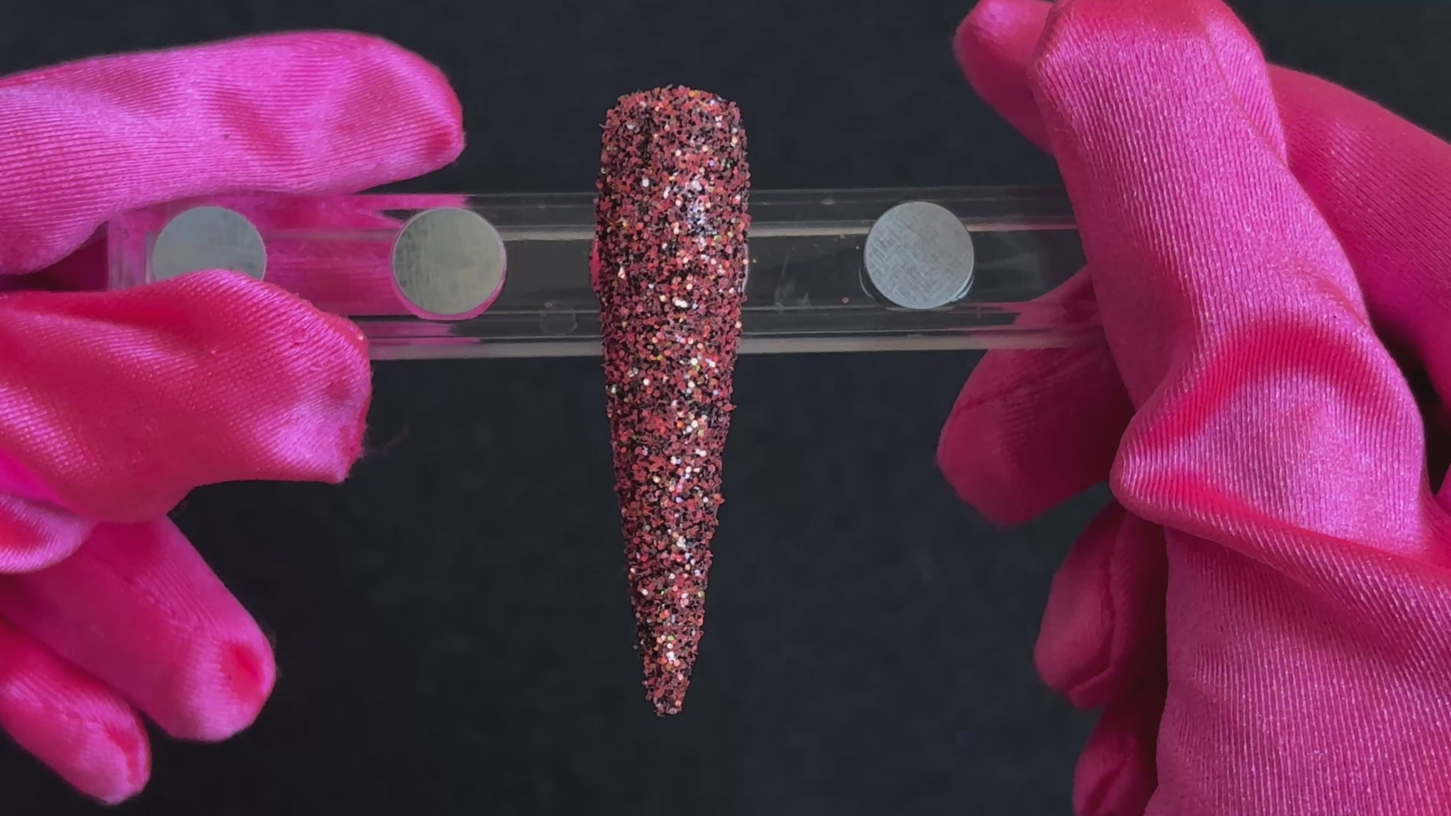 Bright coral and black glitter with holographic and iridescent sparkle applied on a stiletto nail tip, tilted back and forth to show sparkle.