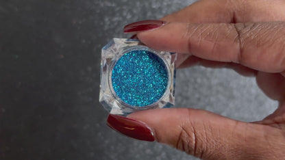 Blue and teal glitter mix in a clear jar, tilted back and forth to show sparkle against a black background.