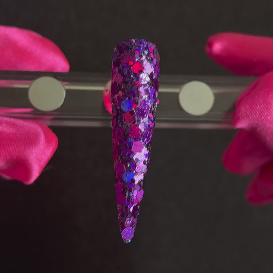 Deep purple and violet super chunky glitter mix with holographic sparkle applied on a stiletto nail tip, tilted back and forth to show sparkle.
