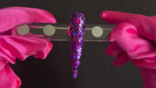 Deep purple and violet super chunky glitter mix with holographic sparkle applied on a stiletto nail tip, tilted back and forth to show sparkle.