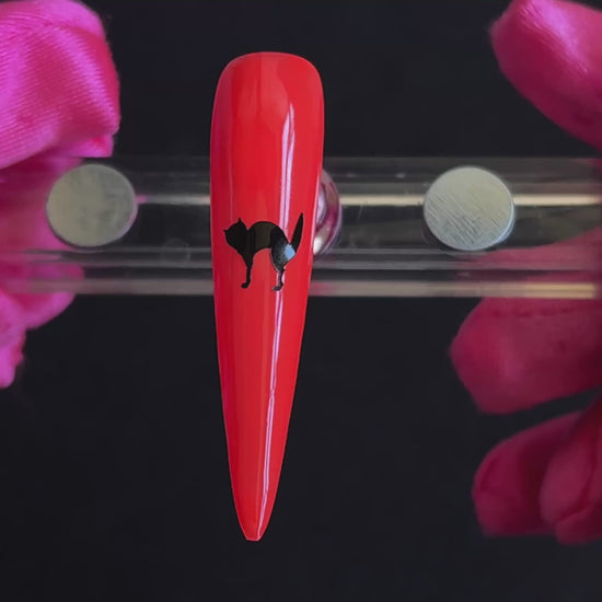 Black cat Halloween nail sticker on a bright orange stiletto nail tip, tilted back and forth to show the finished nail design.