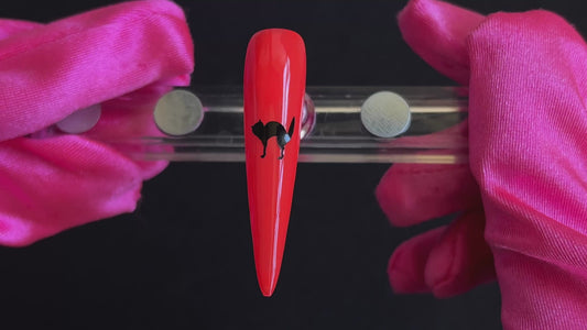Black cat Halloween nail sticker on a bright orange stiletto nail tip, tilted back and forth to show the finished nail design.