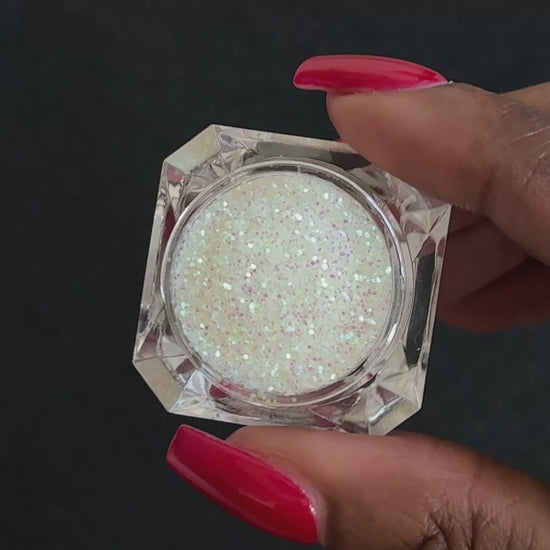 Iridescent white glitter in a clear jar, tilted back and forth to show sparkle against a black background.