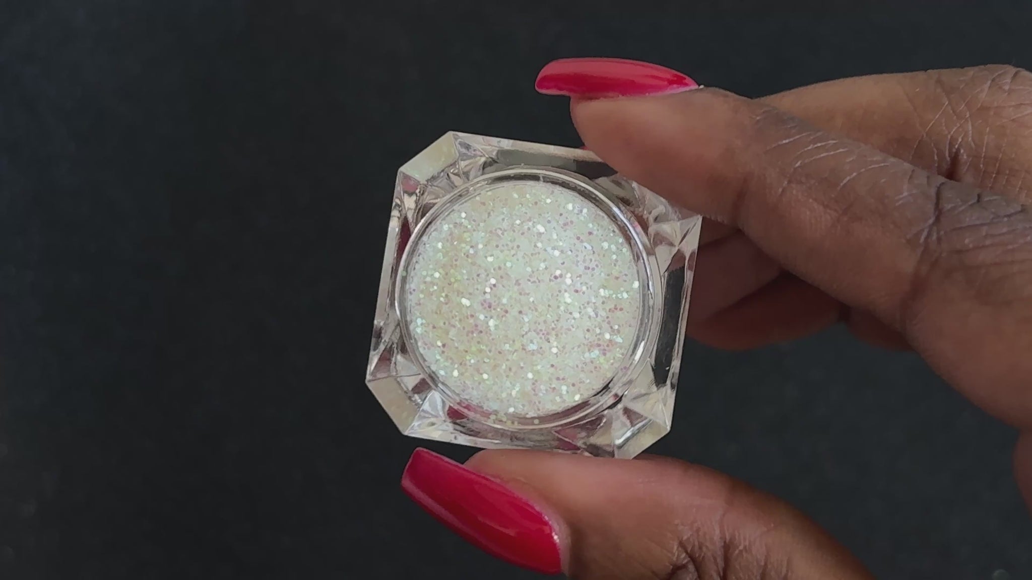 Iridescent white glitter in a clear jar, tilted back and forth to show sparkle against a black background.