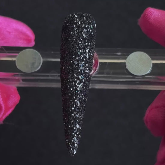 Holographic black glitter applied on a stiletto nail tip, tilted back and forth to show sparkle.
