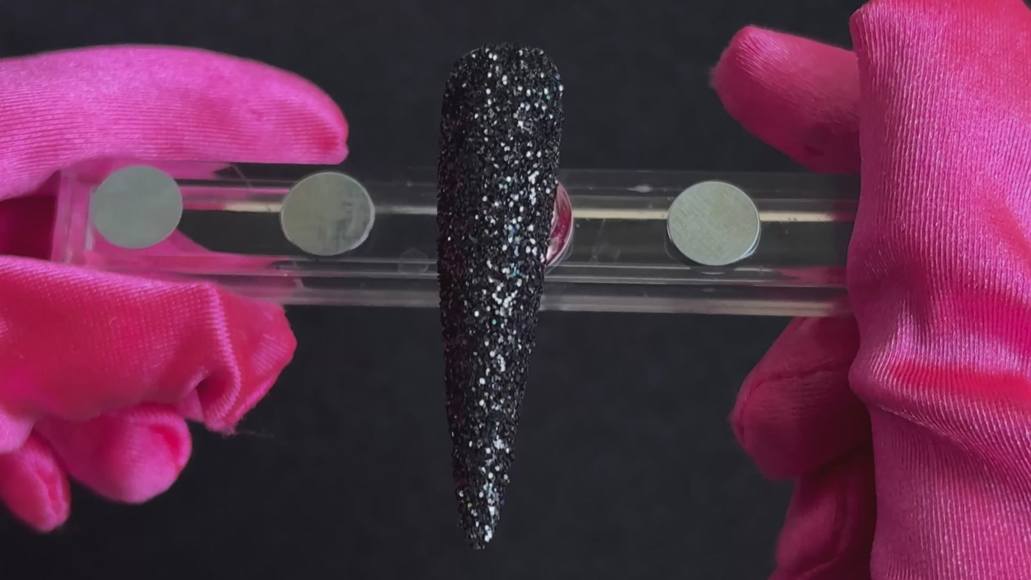 Holographic black glitter applied on a stiletto nail tip, tilted back and forth to show sparkle.