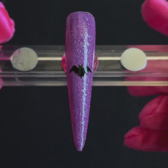 Black bat Halloween nail sticker on a sparkly purple stiletto nail tip, tilted back and forth to show the finished nail design.