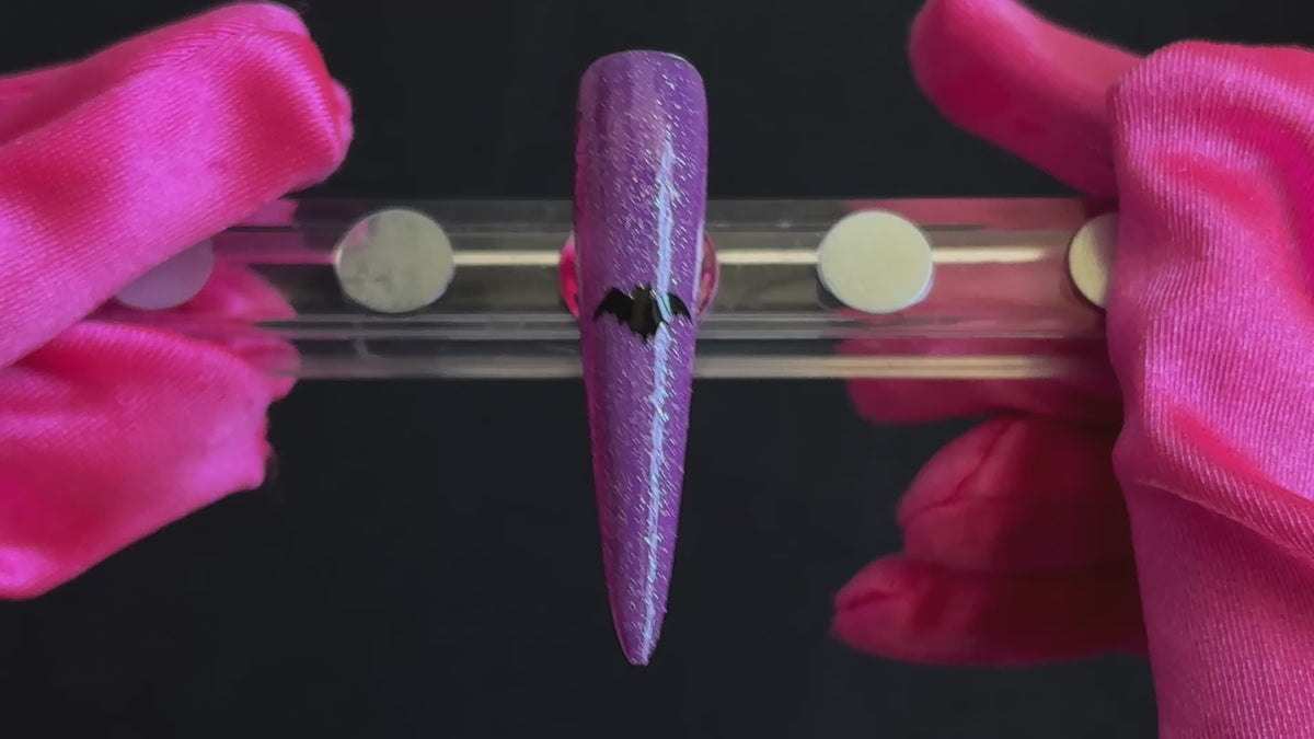 Black bat Halloween nail sticker on a sparkly purple stiletto nail tip, tilted back and forth to show the finished nail design.
