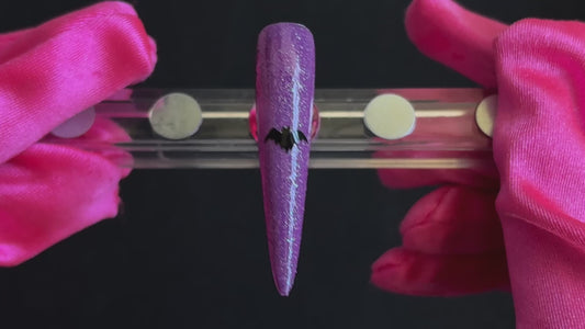 Black bat Halloween nail sticker on a sparkly purple stiletto nail tip, tilted back and forth to show the finished nail design.